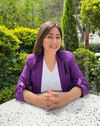 Gina sentada con las manos cruzadas sobre una mesa sonriendo a cámara.